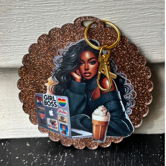Brown glitter resin keychain with scalloped edge featuring an illustration of a stylish Black woman in a sweater, working at a laptop with a “GIRL BOSS” sticker, and a glass of iced coffee. Attached gold keyring and clasp.