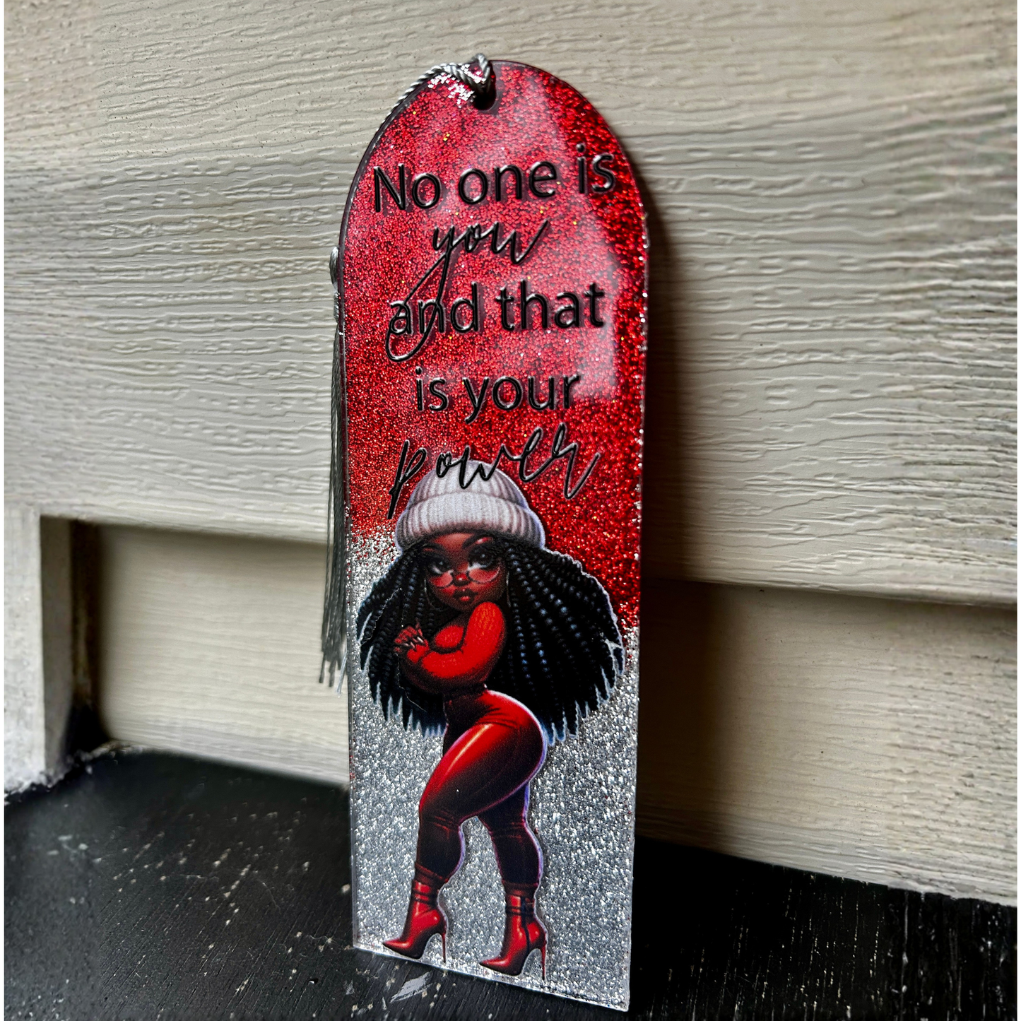Decorative plaque with a woman's silhouette, text, and red background on a wooden surface.