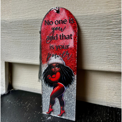 Decorative plaque with a woman's silhouette, text, and red background on a wooden surface.